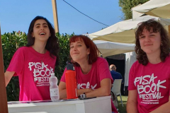 Pisa-book-festival-2023 Foto di tre studentesse a un banchetto del Festival con indosso le magliette del festival